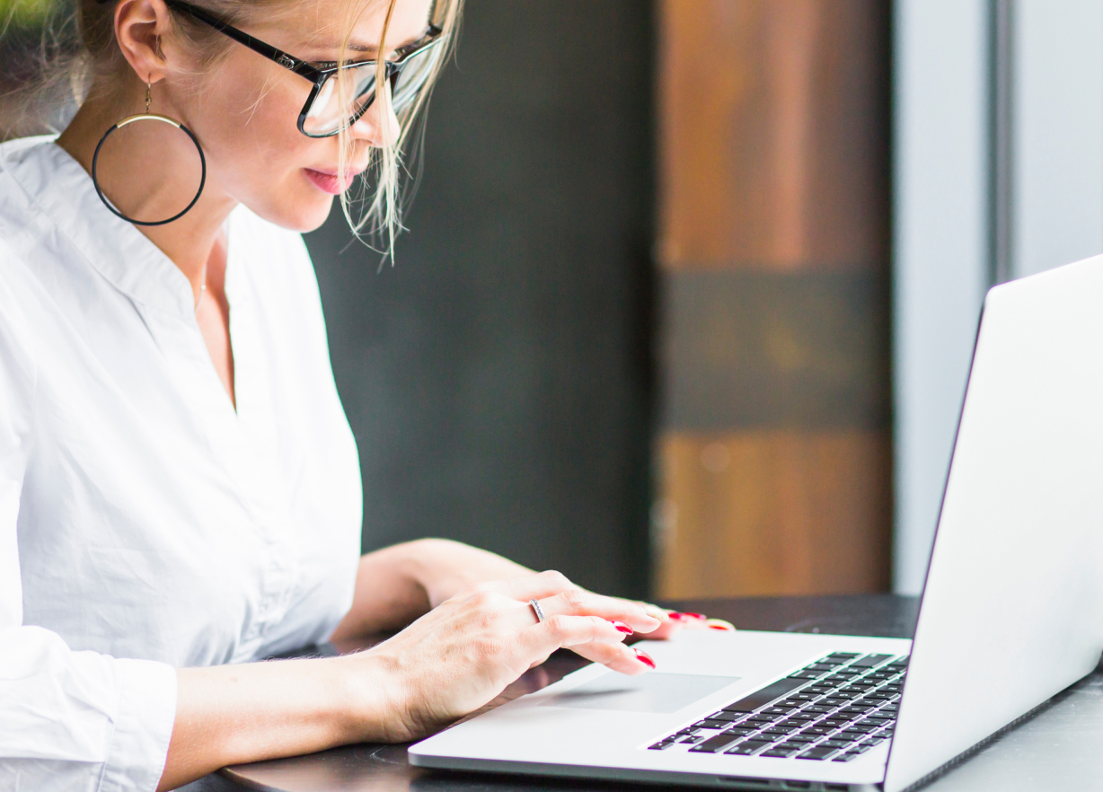 Kobieta w białej koszuli i okularach korekcyjnych podczas pracy przy komputerze.