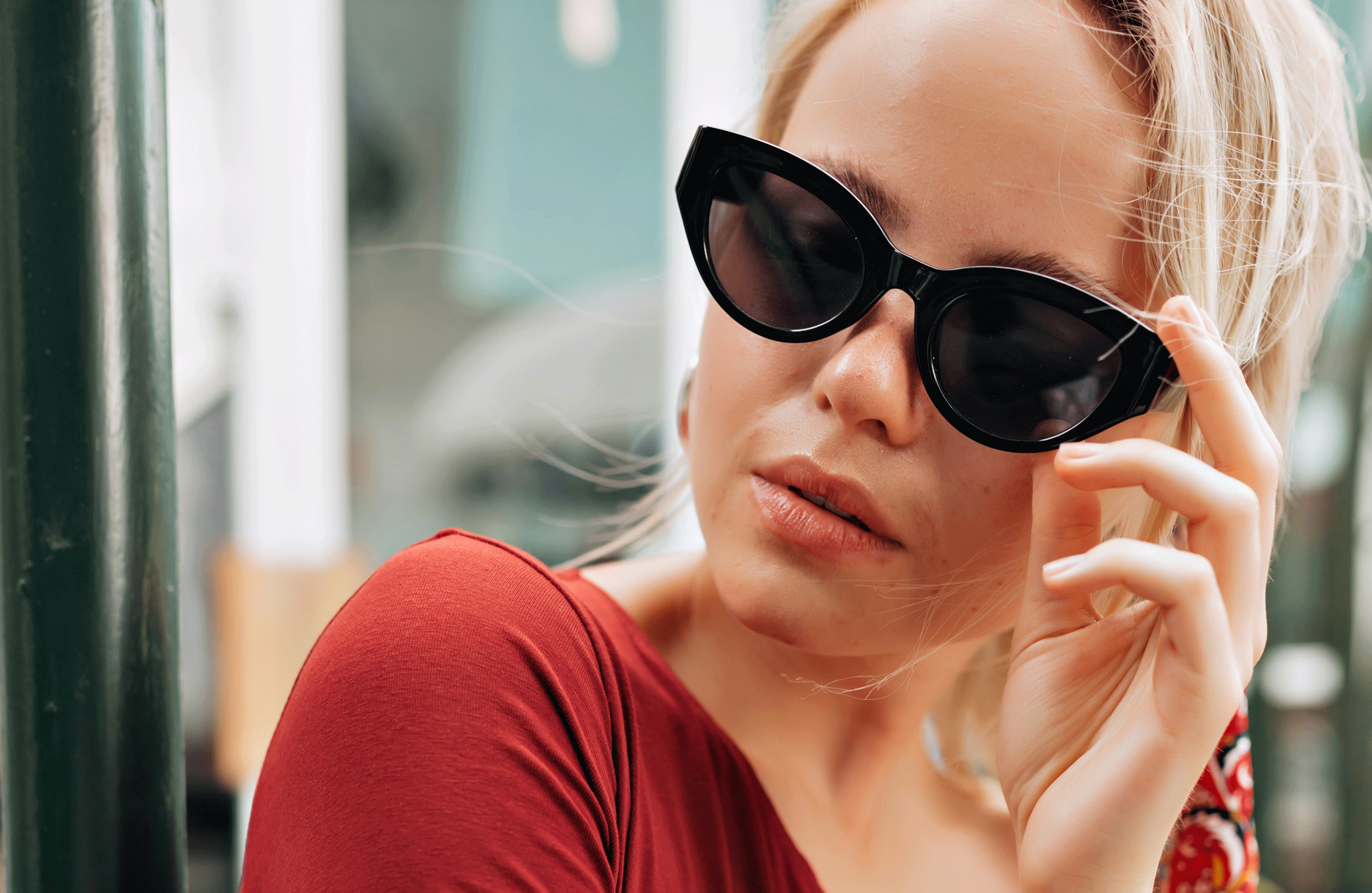 Blondynka w okularach przeciwsłonecznych pozuje do zdjęcia.